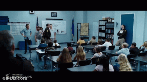 A Group Of People Sitting At Desks In A Classroom With A Sign That Says Movieclips GIF