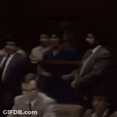 A Group Of People Sitting In A Dark Room With A Man Wearing A Badge That Says ' L.a. ' GIF