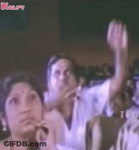 A Group Of People Sitting In A Dark Room With Their Hands In The Air GIF