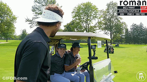 A Group Of People Sitting In A Golf Cart On A Golf Course With Roman Written On The Bottom GIF