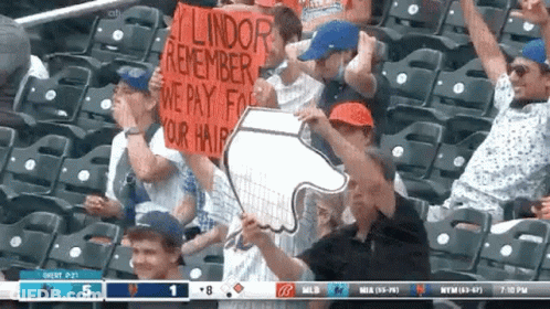A Group Of People Sitting In A Stadium Holding Up Signs That Say Lindor Remember We Pay For Your Hair GIF
