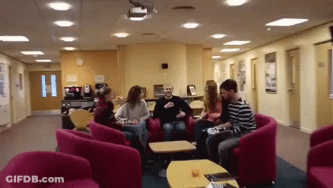 A Group Of People Sitting In Chairs In A Hallway GIF