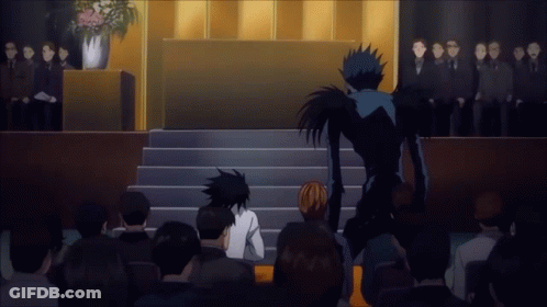 A Group Of People Sitting In Front Of A Podium With A Man In A Black Suit Standing Behind Them GIF