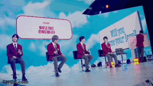 A Group Of People Sitting In Front Of A Sign That Says Will You Me Your GIF