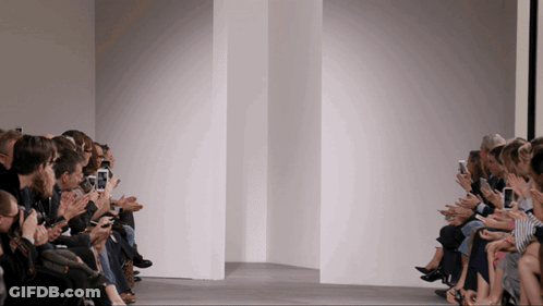 A Group Of People Sitting In Front Of A White Wall Looking At Their Phones GIF