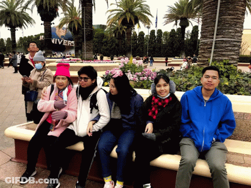 A Group Of People Sitting On A Bench In Front Of A Sign That Says Nivers GIF