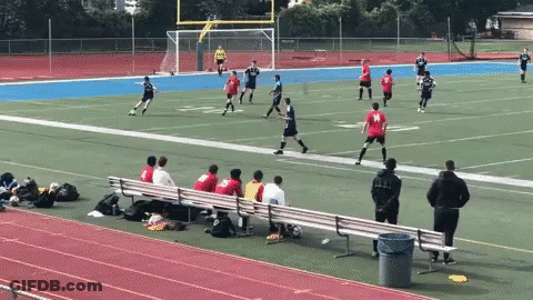 A Group Of People Sitting On A Bench Watching A Soccer Game With A Player Wearing A Red Jersey With The Number 19 On It GIF