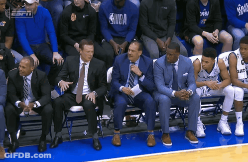A Group Of People Sitting On A Bench With One Wearing A Shirt That Says Nba GIF