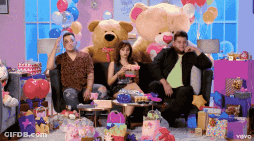 A Group Of People Sitting On A Couch With A Teddy Bear And Balloons In The Background GIF