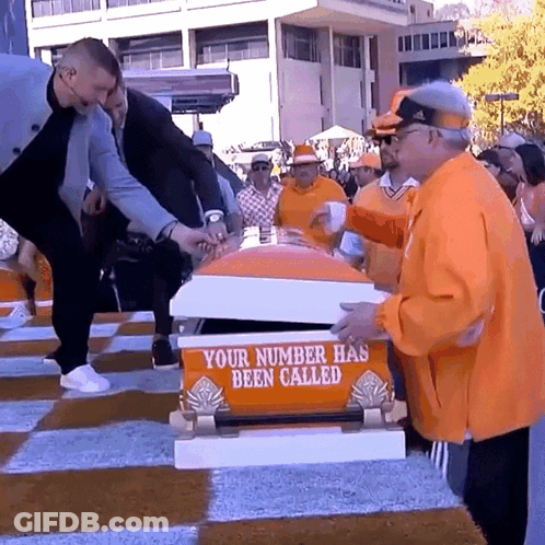 A Group Of People Standing Around A Coffin That Says " Your Number Has Been Called " GIF