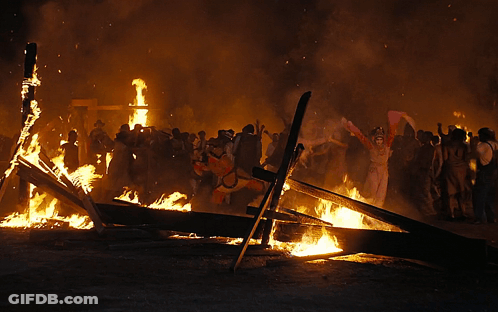 A Group Of People Standing Around A Large Fire GIF