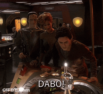 A Group Of People Standing Around A Roulette Table With The Word Dabo On It GIF