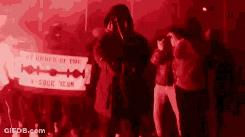 A Group Of People Standing Around A Sign That Says By Order Of The K-Rock Icon GIF
