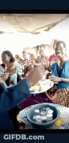 A Group Of People Standing Around A Table Eating Food . GIF
