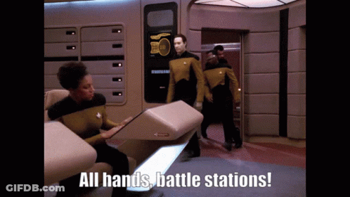 A Group Of People Standing In A Room With The Words " All Hands Battle Stations " On The Bottom GIF