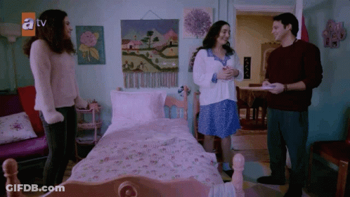 A Group Of People Standing In Front Of A Bed With A TV Logo On The Wall GIF