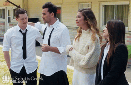A Group Of People Standing In Front Of A Building With #Schitts Creek On The Bottom GIF