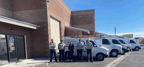A Group Of People Standing In Front Of A Building With Vans Parked In Front Of Them That Say All Kinds Of Plumbing GIF