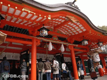 A Group Of People Standing In Front Of A Red Building With Lanterns Hanging From The Ceiling GIF