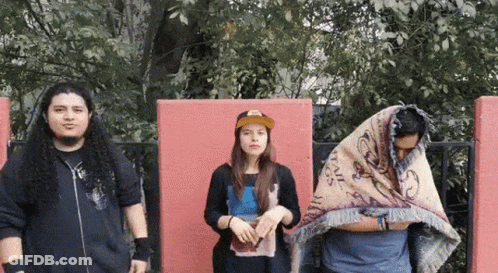 A Group Of People Standing In Front Of A Red Wall Including A Man With A Blanket On His Head GIF