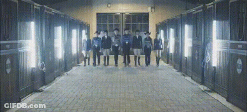 A Group Of People Standing In Front Of A Row Of Stable Doors GIF