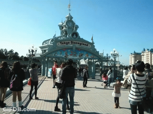 A Group Of People Standing In Front Of A Tokyo Disneyland Gate GIF