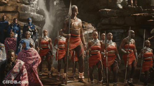 A Group Of People Standing In Front Of A Waterfall With One Woman Holding A Spear GIF