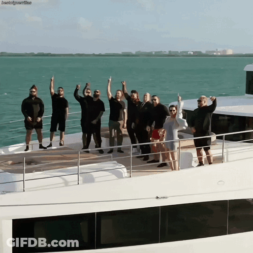 A Group Of People Standing On A Boat With Their Arms Up GIF