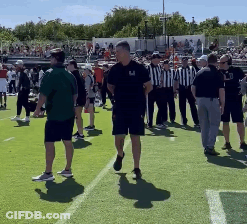A Group Of People Standing On A Football Field With One Man Wearing A Shirt That Says ' Uc ' On It GIF