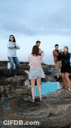 A Group Of People Standing On A Rocky Cliff With A Woman Taking A Picture GIF