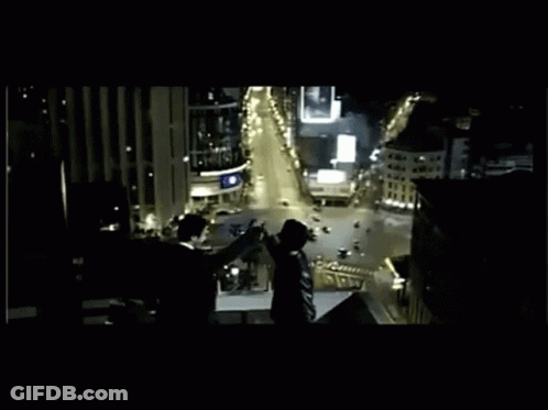 A Group Of People Standing On Top Of A Building Overlooking A City At Night GIF