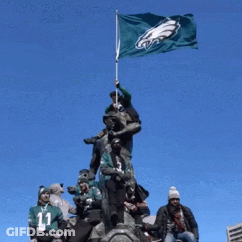 A Group Of People Standing On Top Of A Statue Holding A Flag With The Eagles Logo On It GIF