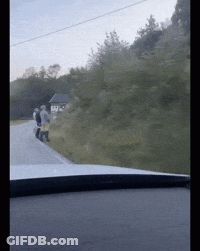 A Group Of People Walking Down A Road With A Small House In The Background GIF