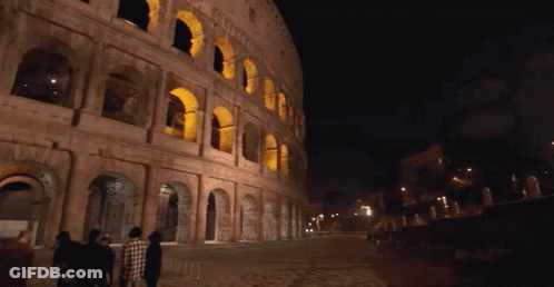 A Group Of People Walking In Front Of A Building That Has Arches On It GIF