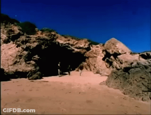 A Group Of People Walking Through A Cave On A Beach GIF