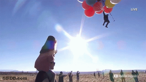A Group Of People Watching A Man Flying Through The Air With Balloons Attached To Him GIF