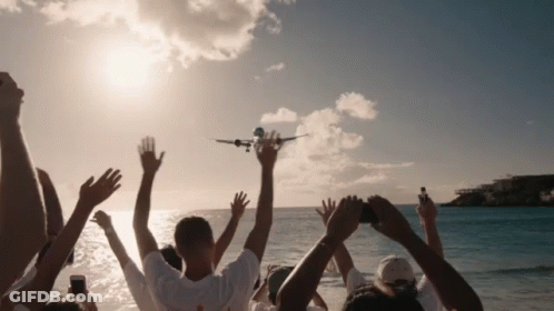 A Group Of People Watching A Plane Taking Off From The Beach GIF