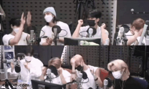 A Group Of People Wearing Face Masks Are Sitting In Front Of Microphones In A Room . GIF