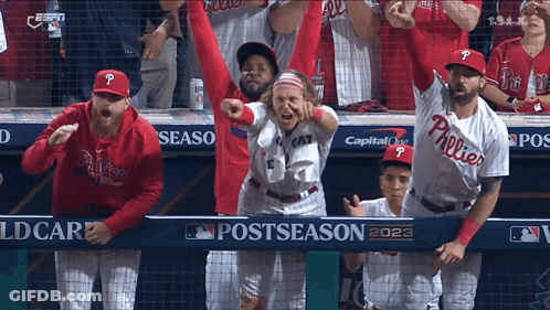 A Group Of Phillies Baseball Players Are Standing In The Dugout With Their Arms In The Air GIF
