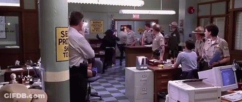 A Group Of Police Officers In A Police Station With A Sign That Says Serve Protect And Serve To Kill GIF