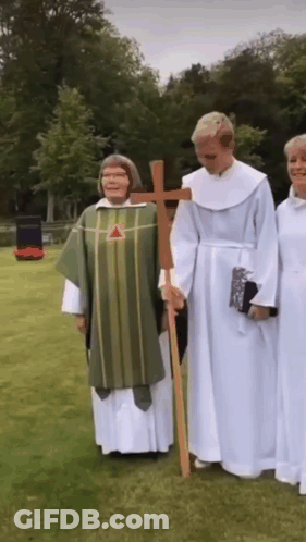 A Group Of Priests Are Standing In A Grassy Field Holding A Cross GIF