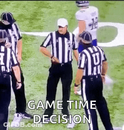 A Group Of Referees Are Standing On A Football Field Talking To A Player . GIF