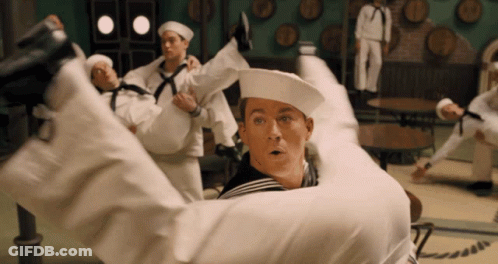 A Group Of Sailors Are Holding A Man In Their Arms In A Room With Barrels On The Wall GIF
