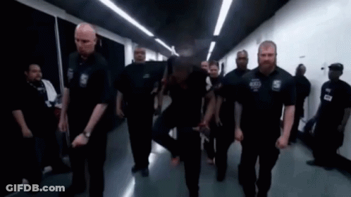 A Group Of Security Guards Are Walking Down A Hallway In A Building . GIF