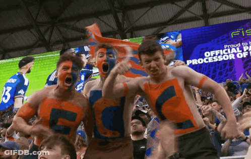 A Group Of Soccer Fans Are Standing In Front Of A Large Screen That Says Proud To Be Official Processor Of GIF