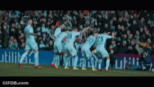 A Group Of Soccer Players Are Celebrating A Goal In Front Of A Sign That Says Utilita GIF