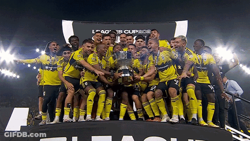 A Group Of Soccer Players Are Holding A Trophy In Front Of A Banner That Says League Cup GIF