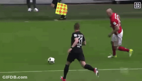 A Group Of Soccer Players Are Playing On A Field With A Referee Holding A Yellow Flag In The Background GIF