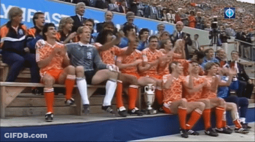 A Group Of Soccer Players Are Sitting On A Bench With A Trophy GIF