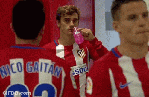 A Group Of Soccer Players Are Standing In A Locker Room Drinking Water From A Pink Bottle . GIF